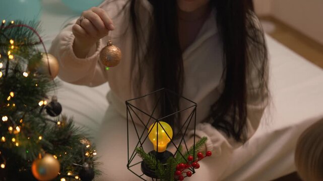 At Christmas, a toddler boy holds gold and black baubles while his mother helps with decorations. The close hands view highlights creative learning, family teamwork and seasonal joy.