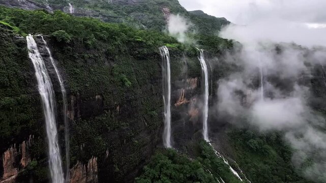 Stunning waterfalls cascading down a lush green mountain cliff in the misty monsoon season