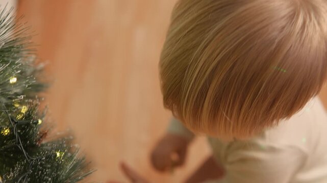 At Christmas, a toddler boy carefully selects a small bauble from Christmas decorations. The close portrait view highlights decision making, independent learning and seasonal joy.