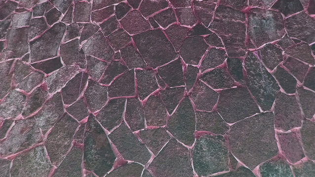 A close-up texture shot of irregular dark stone cladding or crazy paving stonework with distinct pinkish mortar joints, creating a rustic and natural surface pattern.