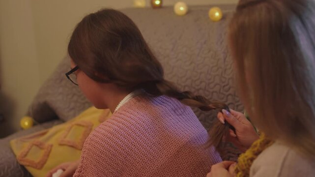 Two young women sit closely together while finishing a handmade Christmas decoration in a festive home. Overhead intimate view captures warm companionship for authentic Christmas storytelling.