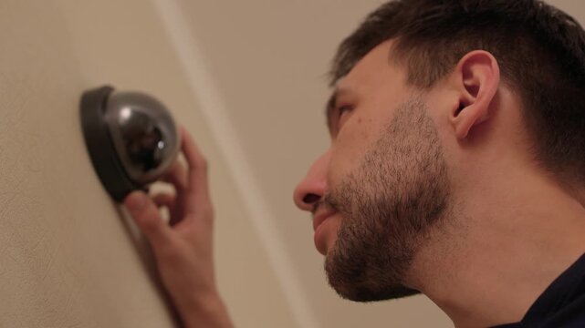 Technician installs indoor dome camera. Camera technician secures mounting and tests wiring. Security system installer calibrates lens and adjusts wiring carefully