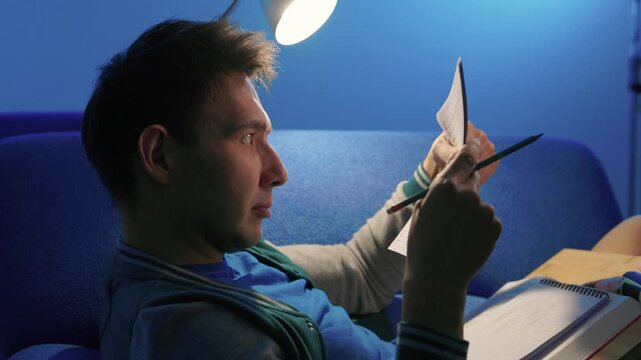 Individual concentrates while reviewing documents quietly. Lone individual carefully examines handwritten notes under gentle illumination during late night hours at home