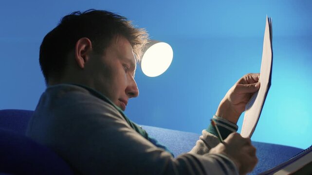 Individual concentrates while reviewing documents quietly. Lone individual carefully examines handwritten notes under gentle illumination during late night hours at home