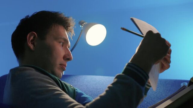 Individual concentrates while reviewing documents quietly. Lone individual carefully examines handwritten notes under gentle illumination during late night hours at home