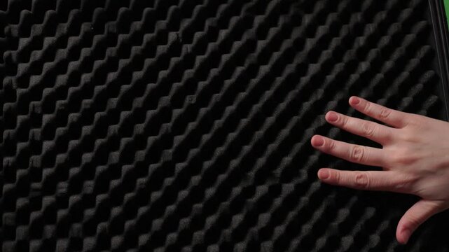 Hand touching foam rubber soundproofing panel, closeup texture study with soft studio light and eggcrate pattern conveying tactile curiosity and acoustic control