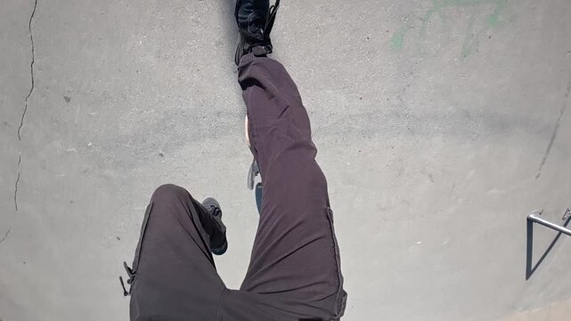 A skateboarder is missing a trick in POV and falling on the ground in a skatepark on a sunny day, super slow motion