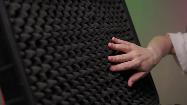 Hand touching foam rubber soundproofing panel, closeup texture study with soft studio light and eggcrate pattern conveying tactile curiosity and acoustic control