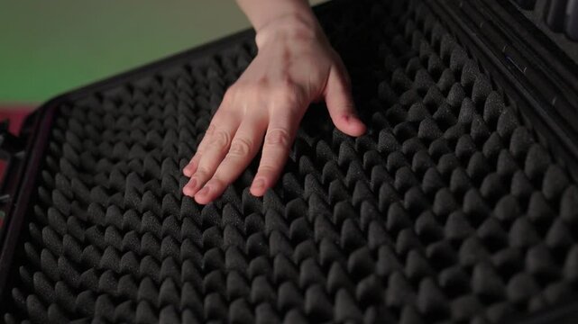 Hand touching foam rubber soundproofing panel, closeup texture study with soft studio light and eggcrate pattern conveying tactile curiosity and acoustic control
