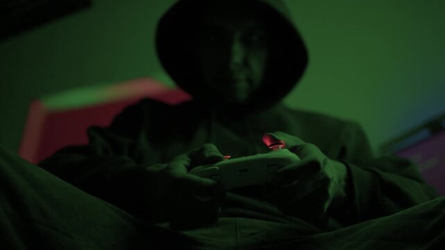 Gamer gripping red controller in dark hoodie, lowlit room with neon green PC and blurred monitor, closeup on hands and controller, tense focused mood, latenight stream atmosphere