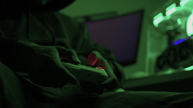 Gamer gripping red controller in dark hoodie, lowlit room with neon green PC and blurred monitor, closeup on hands and controller, tense focused mood, latenight stream atmosphere