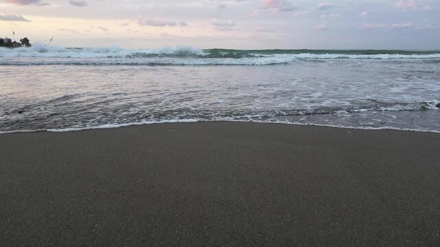 Static ground-level slow motion view of a gentle ocean wave washing onto a sandy beach, capturing the natural rhythm of the shoreline.
