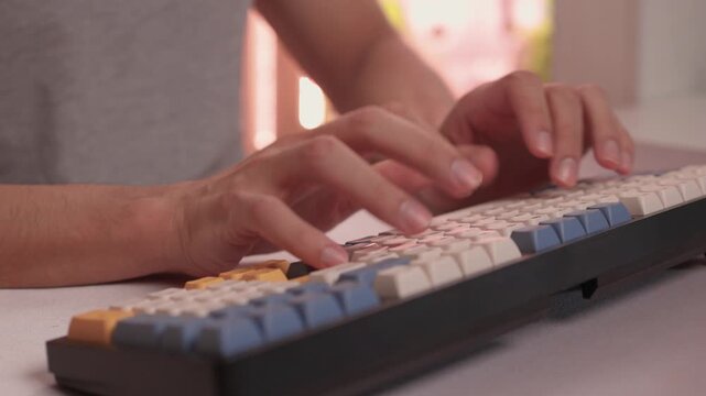 Typing in warm ambient light. Steady rhythm while coding with colorful keycaps at night. Closeup of hands working on keyboard under soft lighting with bokeh background