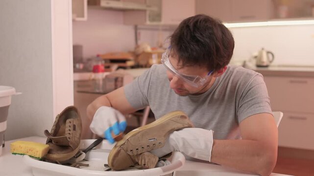 Gloved hands scrubbing suede boots, closeup of sponge lathering dirt and salt stains, patient circular motions, basin with foam, warm indoor lighting, home care scene