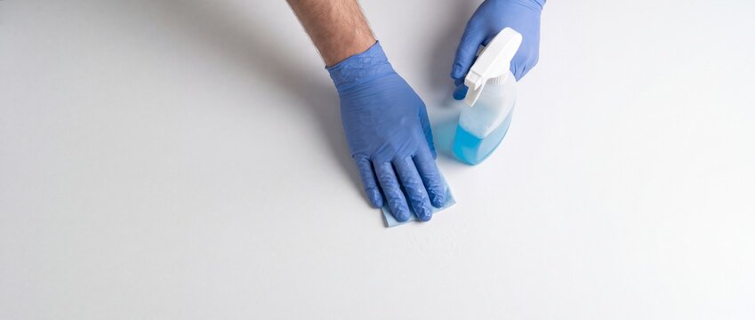 Person wearing blue gloves wiping a white surface with a spray cleaner