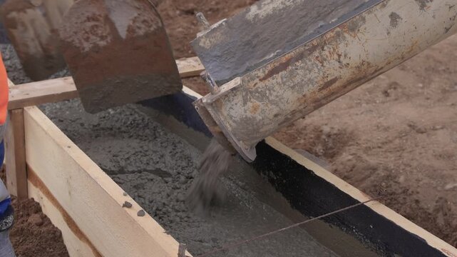 Construction worker actively pouring concrete into forms. Construction worker skillfully pouring wet concrete into formwork amid surrounding earth and safety gear