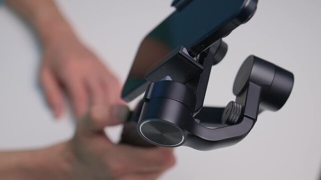 Person adjusts camera stabilizer while smiling in professional studio setup. Person in casual attire is testing camera movement techniques in blue studio environment