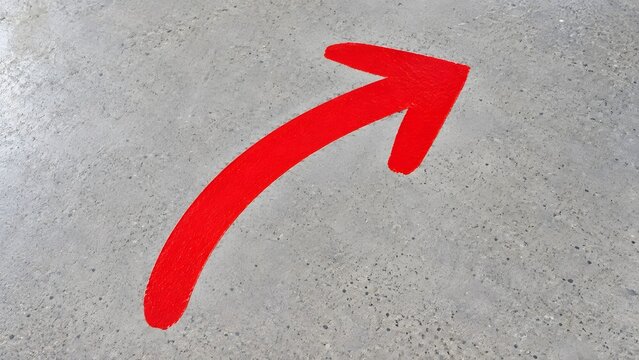 Bright red directional arrow painted on textured concrete floor indicating direction upwards and to the right simple graphic symbol for guidance and movement
