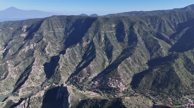 Aerial pan left over the remote hamlet of Los Loros with a water dam, nestled in the rugged, lush mountains of La Gomera (Canary Islands), revealing stunning natural beauty.