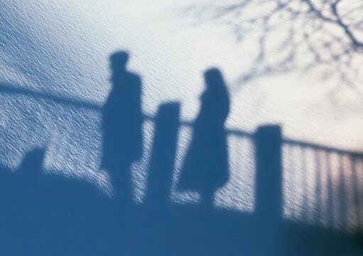 Silhouetted figures cast long shadows on a textured surface near water