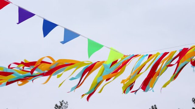 Bright red, yellow, and blue streamers flutter diagonally against a soft sky, creating a festive mood. Traditional Maslenitsa festivities	
