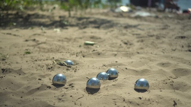 Metal Balls Fall onto Sand. Beach Petanque Game in Sunny Weather. Players metal balls fall onto sand during a petanque game on the beach, sunny day, outdoor sports atmosphere.