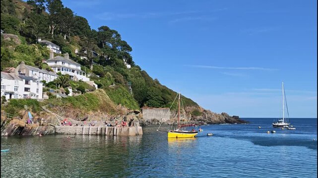Polperro Cornwall England UK. 20.08.2026. Video. Small yacht under power approaching the scenic resort of Polperro harbour against a blue summer sky.