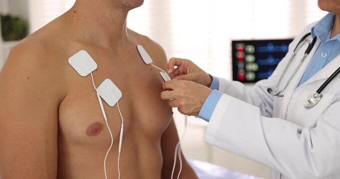 Doctor attaching ECG electrodes to patient's chest in clinic, closeup