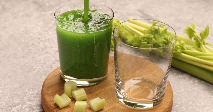Woman pouring fresh celery juice into glasses at grey table, closeup