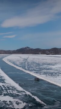 Drone footage of a vehicle driving along a cleared ice road across frozen Lake Baikal in winter, with snow patterns, blue ice and distant mountains, Russia