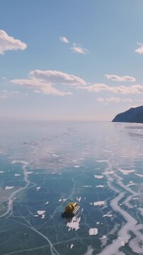 Aerial view of a hovercraft traveling across cracked blue ice on Lake Baikal in Siberia, Russia, with snowy shoreline and mountains on a clear winter day