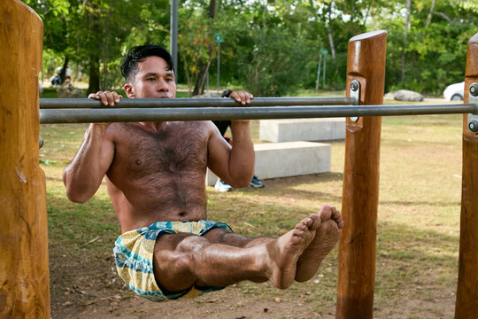 Man doing calisthenics workout and pull-ups on parallel bars in a public park