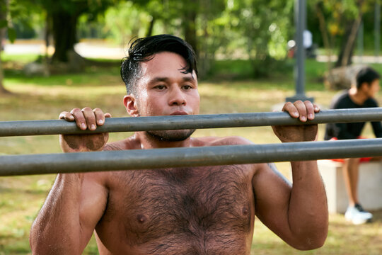 Man doing calisthenics workout and pull-ups on parallel bars in a public park