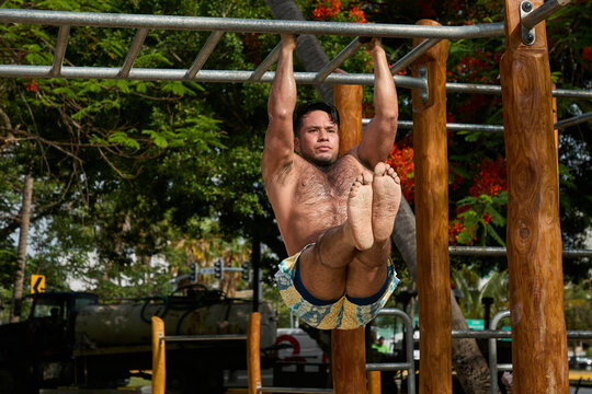 Man doing calisthenics workout and pull-ups on parallel bars in a public park