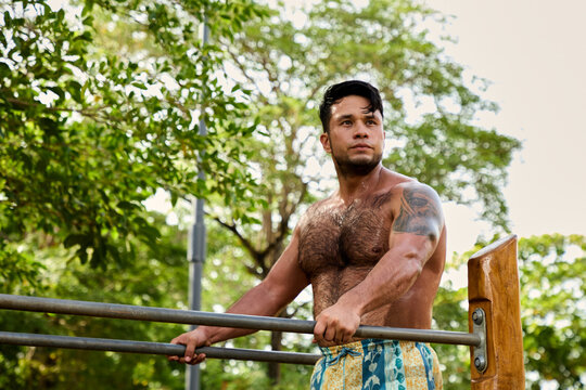 Man doing calisthenics workout and pull-ups on parallel bars in a public park
