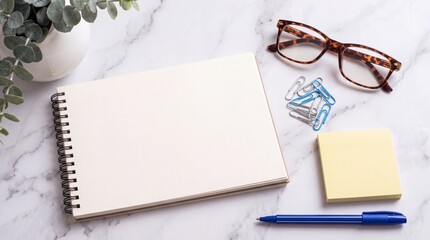 Obraz premium Top down view of an empty blank spiral notebook on a modern white marble desk surface with stylish glasses, blue pen, yellow sticky notes, colorful paperclips, and a green potted plant.