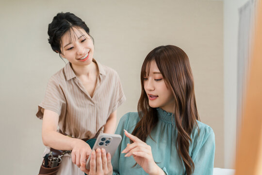 美容室でスマホを見ながら相談する女性客と美容師。ヘアスタイルを選ぶカウンセリング