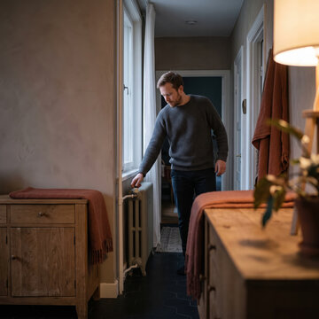 Young man adjusting the thermostat knob on a vintage heating radiator at home in winter