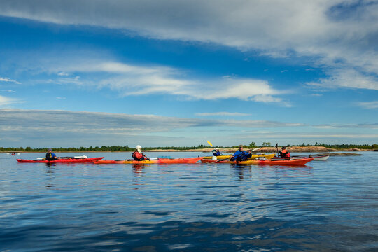 Group of sea kayakers lined up on calm reflective water on a sunny morning under a cloud-streaked blue sky, copy space, Georgian Bay, Ontario