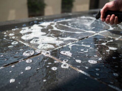 Close up of stone tile terrace patio floor cleaning process with white soapy foam and pressure water sprayer wand.