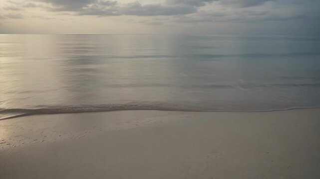 Nature - Calm sea waves gently rolling onto a clean white sandy beach during a serene overcast morning sunset