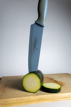 Fresh zucchini with a cut slice and kitchen knife on a wooden cutting board, vertical close-up of healthy vegetable preparation and home cooking.