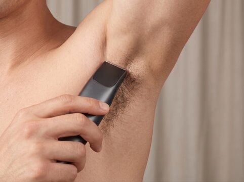 A man using an electric trimmer to shave hair from his underarm area for personal grooming needs.