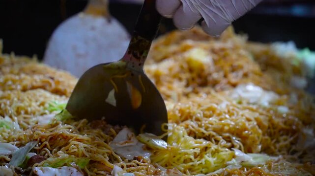 cinematic close-up shot of a chef using metal spatulas to stir-fry a massive amount of yakisoba noodles on a hot flat iron griddle at a japanese street food stall