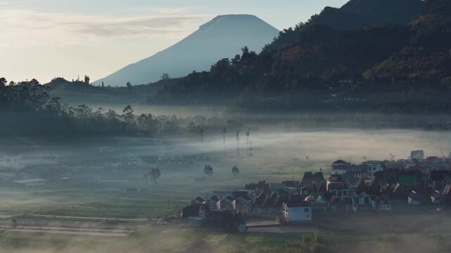Aerial view of dieng plateau with volcano rising above a misty valley and a small village nestled in the landscape in Indonesia. 