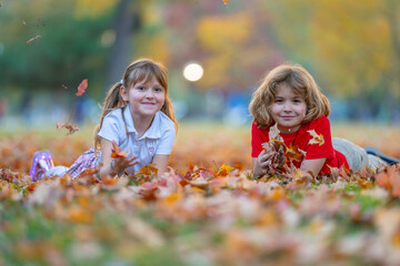 Obraz premium Autumn leaves near happy kids. Children smile on fallen foliage. Leaves fly during tossing. Play brings carefree fun. Laughing girl looks at boy. Friendship scene in park.