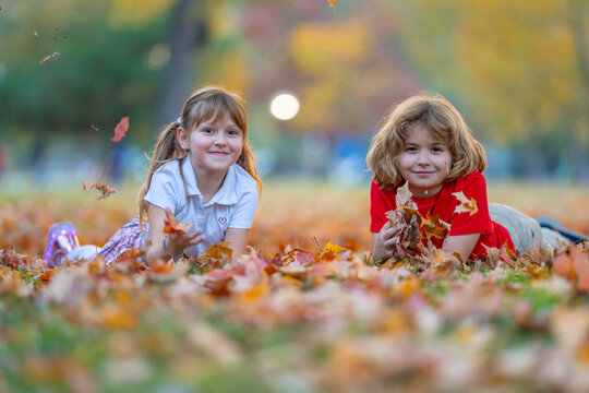 Autumn leaves near happy kids. Children smile on fallen foliage. Leaves fly during tossing. Play brings carefree fun. Laughing girl looks at boy. Friendship scene in park.