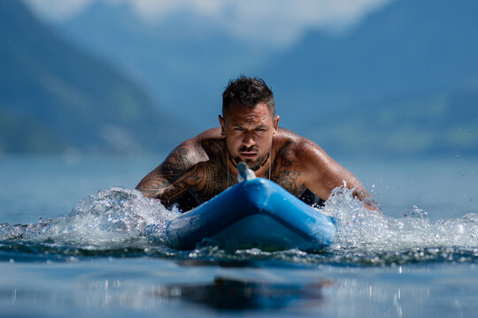 SUP rider with paddle against Alps scenery. Shirtless SUP paddler on mountain lake. SUP recreation during active summer travel. Muscular man on SUP in nature.