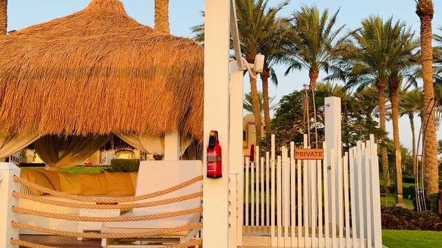 VIP cabana luxury bungalow with straw roof and white private pergola at Sharm El Sheikh hotel resort in Egypt. Beautiful beach canopy on sunny day background with green palm trees, tropical view