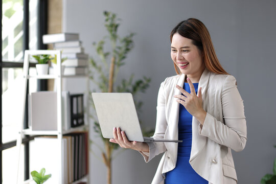 Smiling businesswoman using laptop making video conference call, e-learning, online training, studying, working from home, having virtual meeting or webinar, looking at computer screen, waving hand.